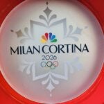 A promotional sign for the Milan Cortina Olympic Games 2026, featuring the NBC peacock logo.