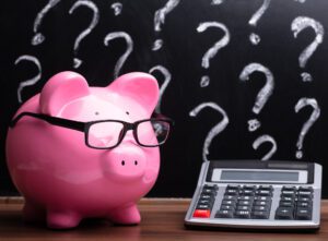 Close-up Of A Pink Piggybank With Eyeglasses And Calculator On Wooden Desk